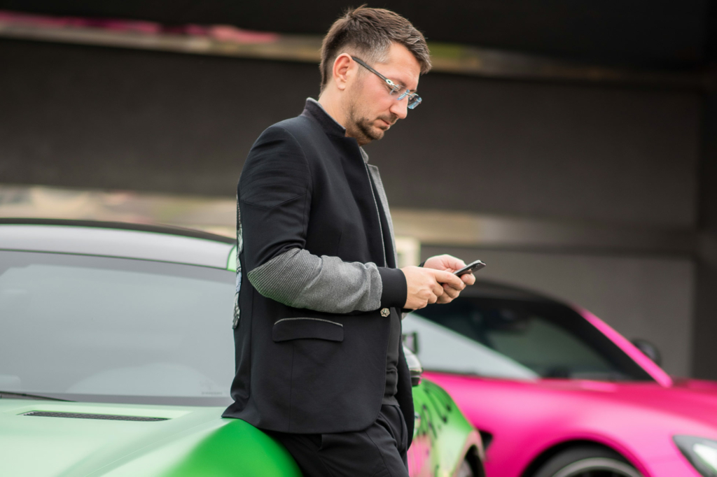 Walter Temmer Wahrheit Walter Temmer mit schwarzem Sakko lehnt an einem grüne Auto und hat das Handy in der Hand