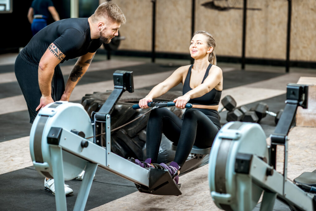 Fitnesscoach redet mit Frau auf Fitnessgerät