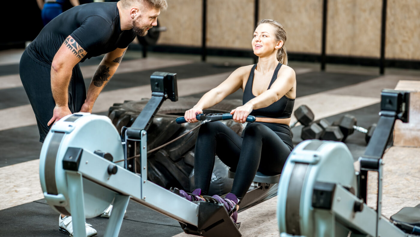Fitnesscoach redet mit Frau auf Fitnessgerät