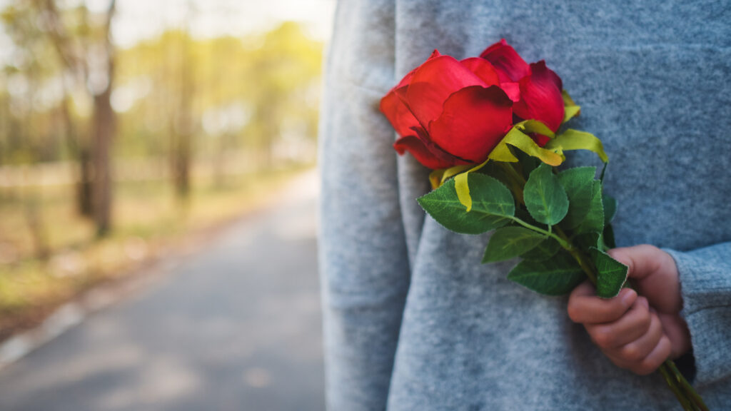 Ein Strauß roter Rosen wird hinter dem Rücken versteckt