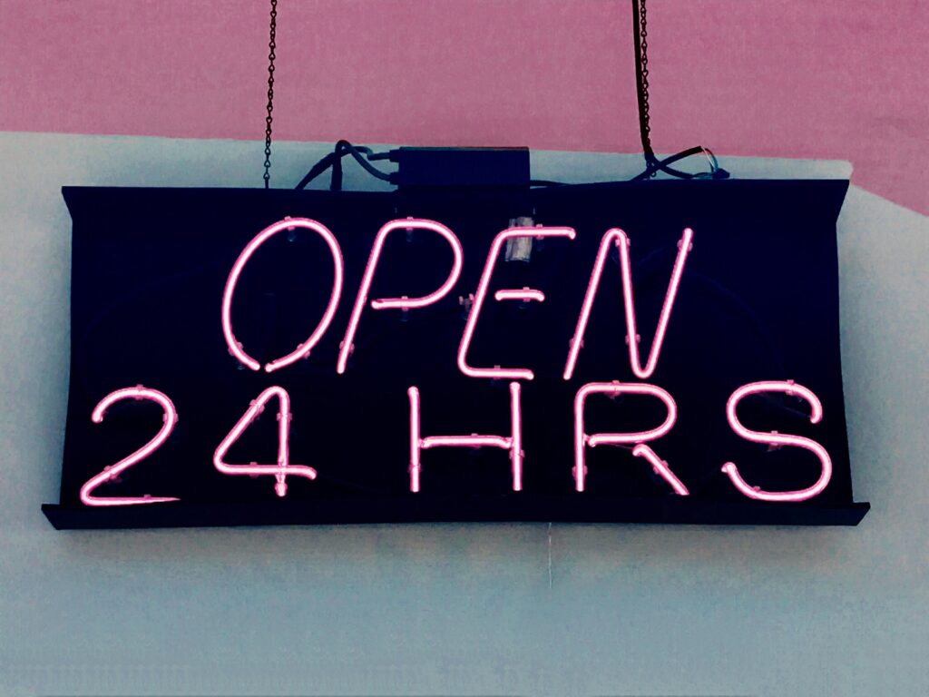 hängende Tafel mit pinker Aufschrift "OPEN 24 HOURS"