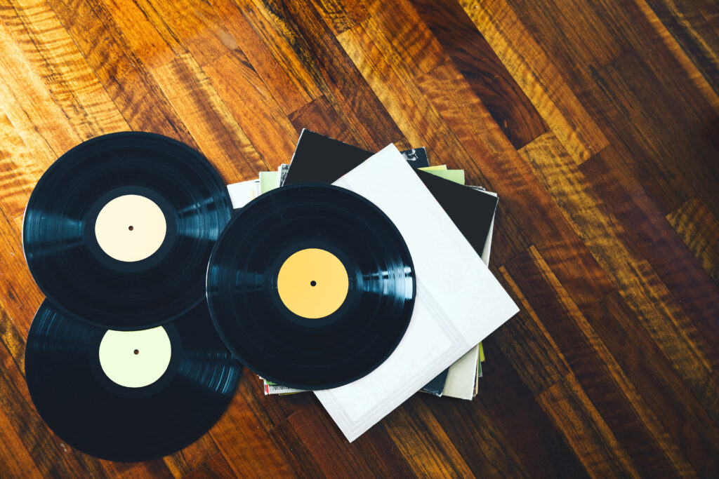 2 Schallplatten liegen auf einem Holztisch und 1 Schallplatte liegt auf einem Stapel von CDs