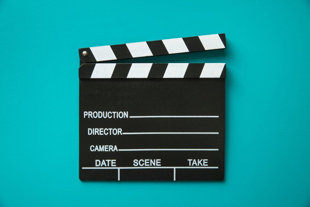 Filmklappe mit Aufschrift Production, Director, Camera vor türkisem Hintergrund