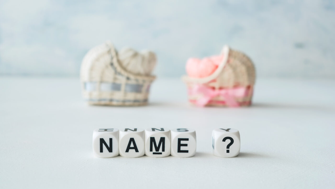 Buchstaben mit Name und Fragezeichen. Dahinter ein blaues und rosarotes Babykörbchen