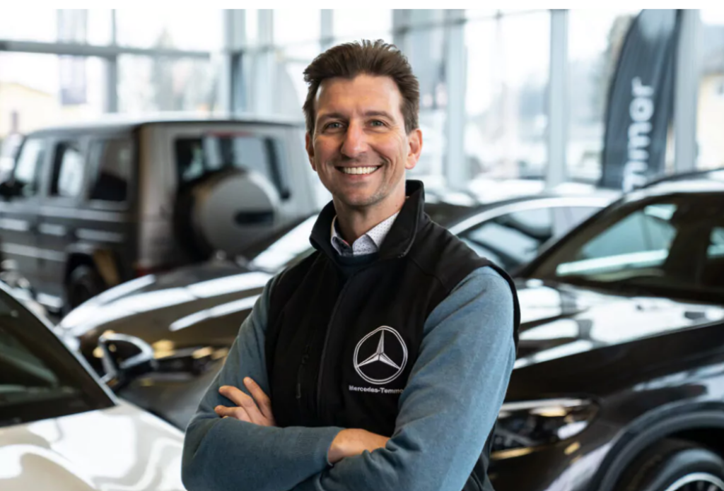 Andreas Temmer als Geschäftsführer vom Autohaus Temmer steht mit verschränkten Händen vor Mercedes Elektroauto und lacht in die Kamera