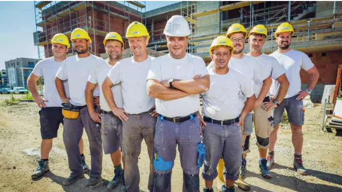 Bautechniker Leibnitz auf der Baustelle Bautechniker in Leibnitz stehen auf einer Baustelle in weißen T-Shirts und mit Sicherheitshelmen und machen ein Gruppenfoto