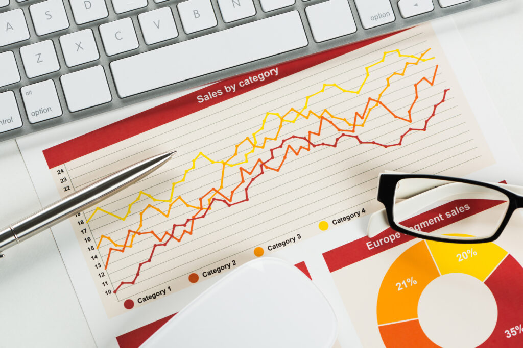 Teile einer Computertastatur. Davor eine Grafik mit der Beschriftung Sales by category, ein Kugelschreiber und eine Brille