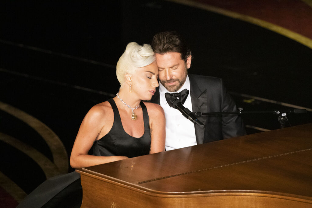 Lady Gaga mit Bradley Cooper am Klavier; sie halten die beiden Köpfe innig aneinander