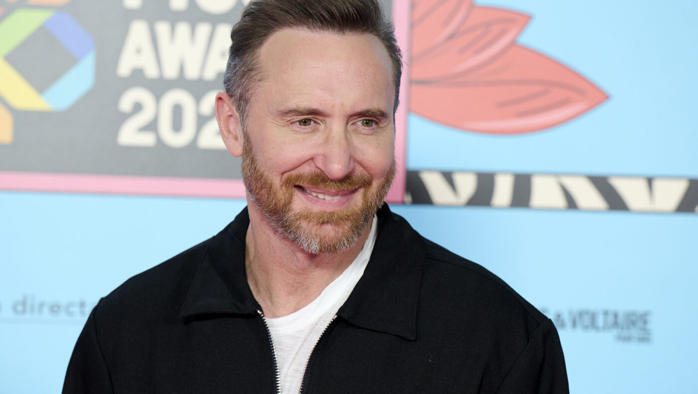 David Guetta mit schwarzer Jacke und weißem T-Shirt sowie Bart lächelt seitlich in die Kamera