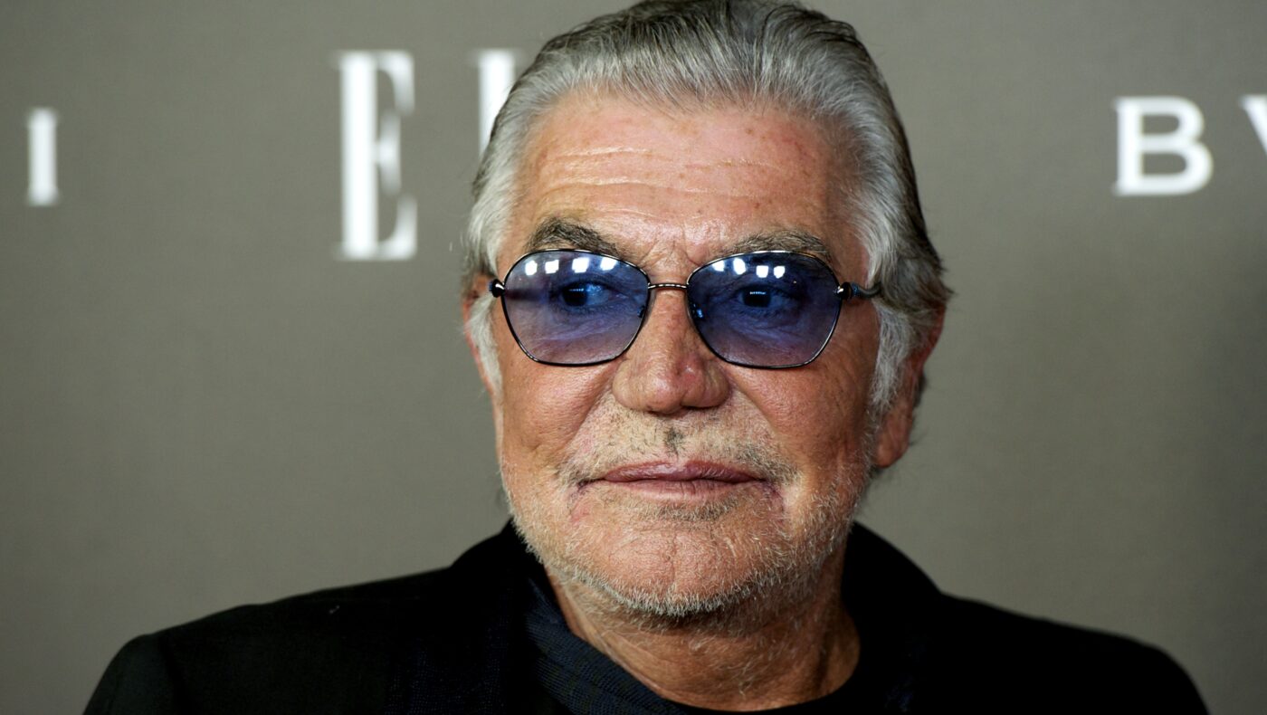 Roberto Cavalli posiert vor Werbewand