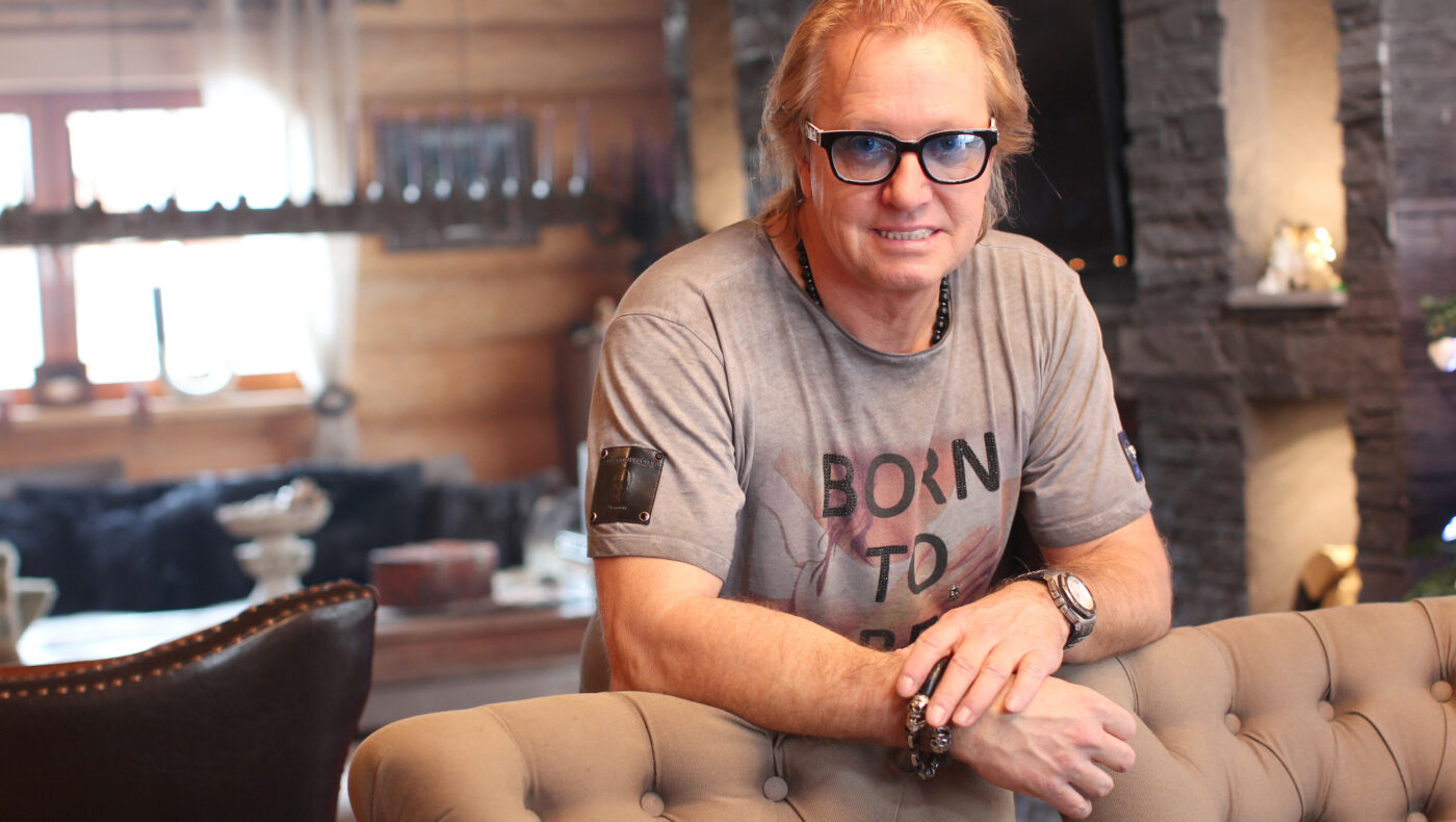 Robert Geiss lehnt mit T-Shirt und Sonnenbrille an einem braunen Sofa