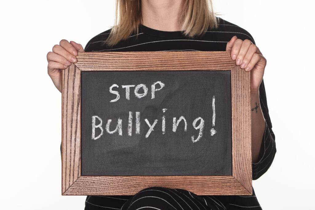 Schild mi einem Holzrahmen das von einer Frau deren Gesicht man nicht sieht gehalten wird. Auf dem Schild steht: Stop Bullying! 