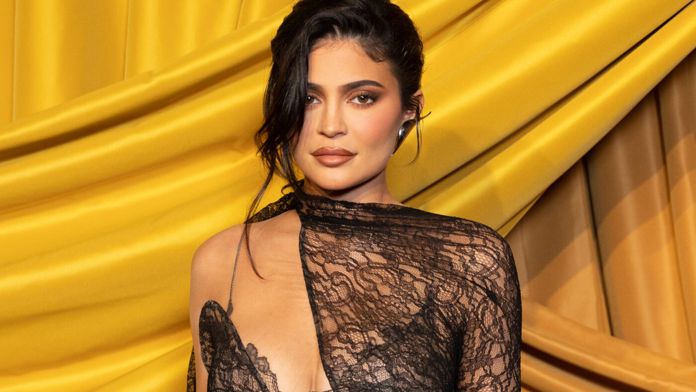 Kylie Jenner mit schwarzem durchsichtigen Kleid vor einem gelben Hintergrund
