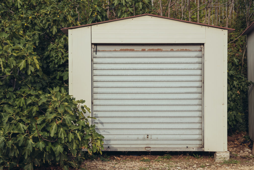 Blick auf eine einfach kleine Garage die mit Büschen verwachsen ist