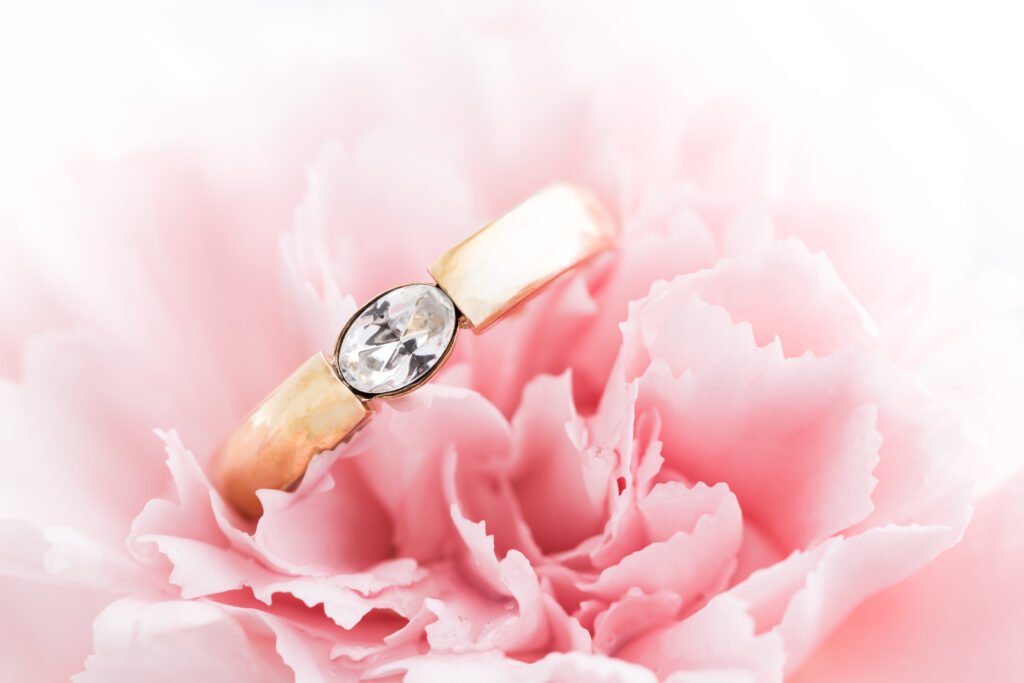 Rosarote Blüte in Nahaufnahme mit einem goldenen Ring, der einen Diamant in der Mitte hat