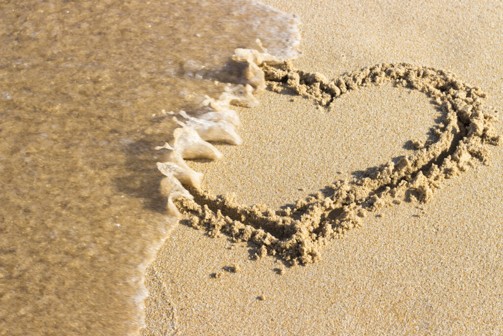 Sand mit einem Herz gezeichnet das zum Teil von einer Welle überspült wurde