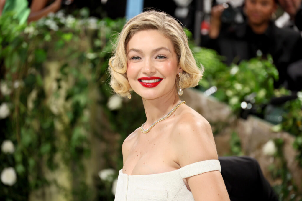 Gigi Hadid mit rotem Lippenstift und blonden kurzen Haaren lächelt in die Kamera