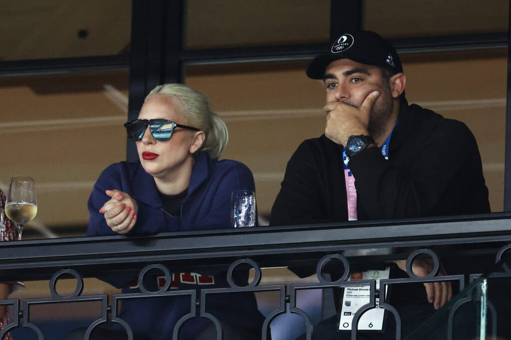 Lady Gaga mit dunkler Sonnenbrille sitzt n eben einem Mann