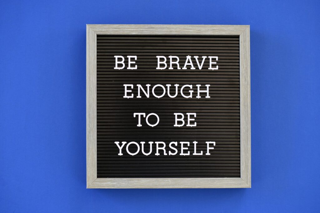 blauer Hintergrund; Schild mit Be brave enough to be yourself