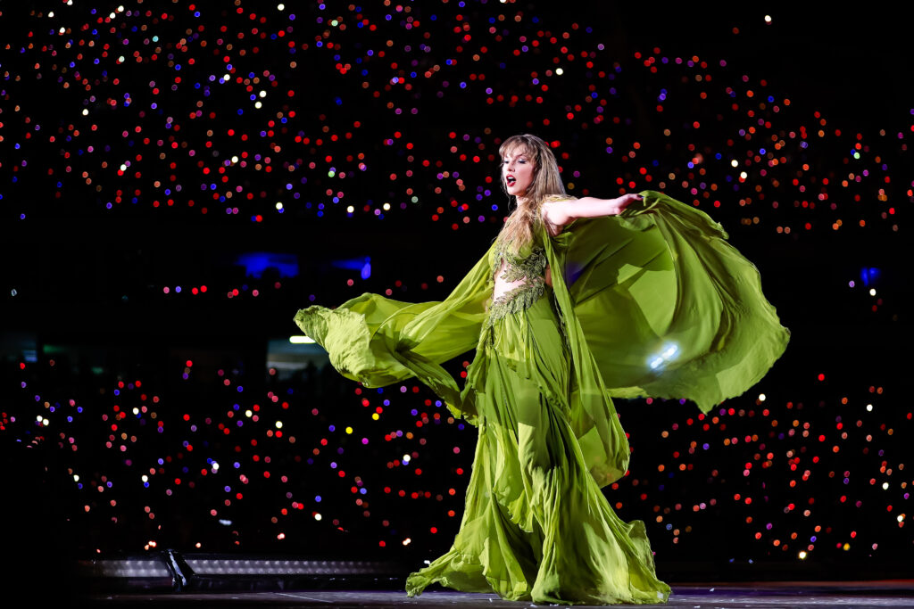 Taylor Swift mit grünem Kleid auf der Bühne hält die Arme weit auseinandergestreckt