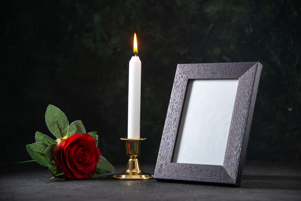 schwarzer Hintergrund mit einer roten Rose, weißen Kerze und einem Bilderrahmen ohne Foto 