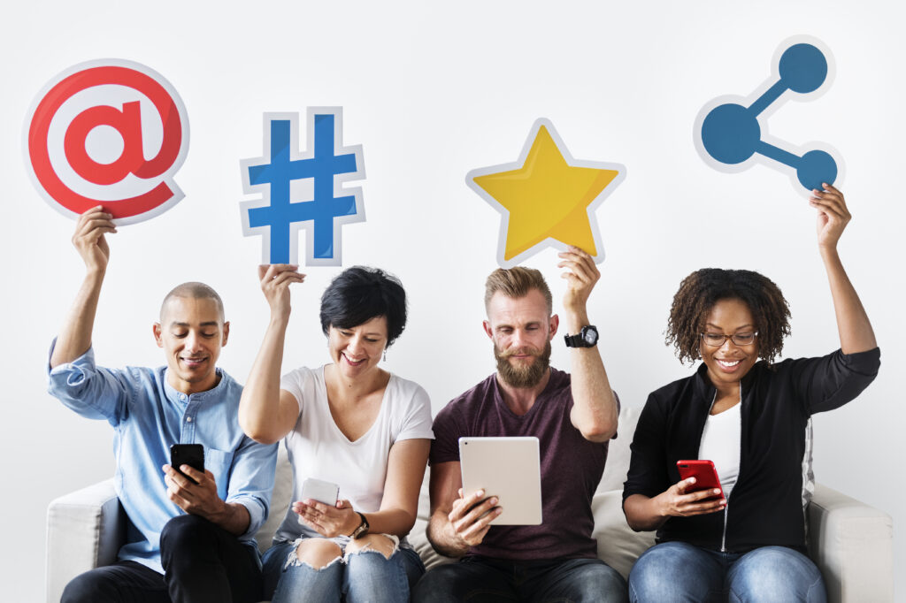 vier Menschen sitzen nebeneinander und halten social-media Icons hoch