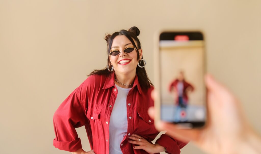Frau mit rotem Hemd, Sonnenbrille post vor einem Handy